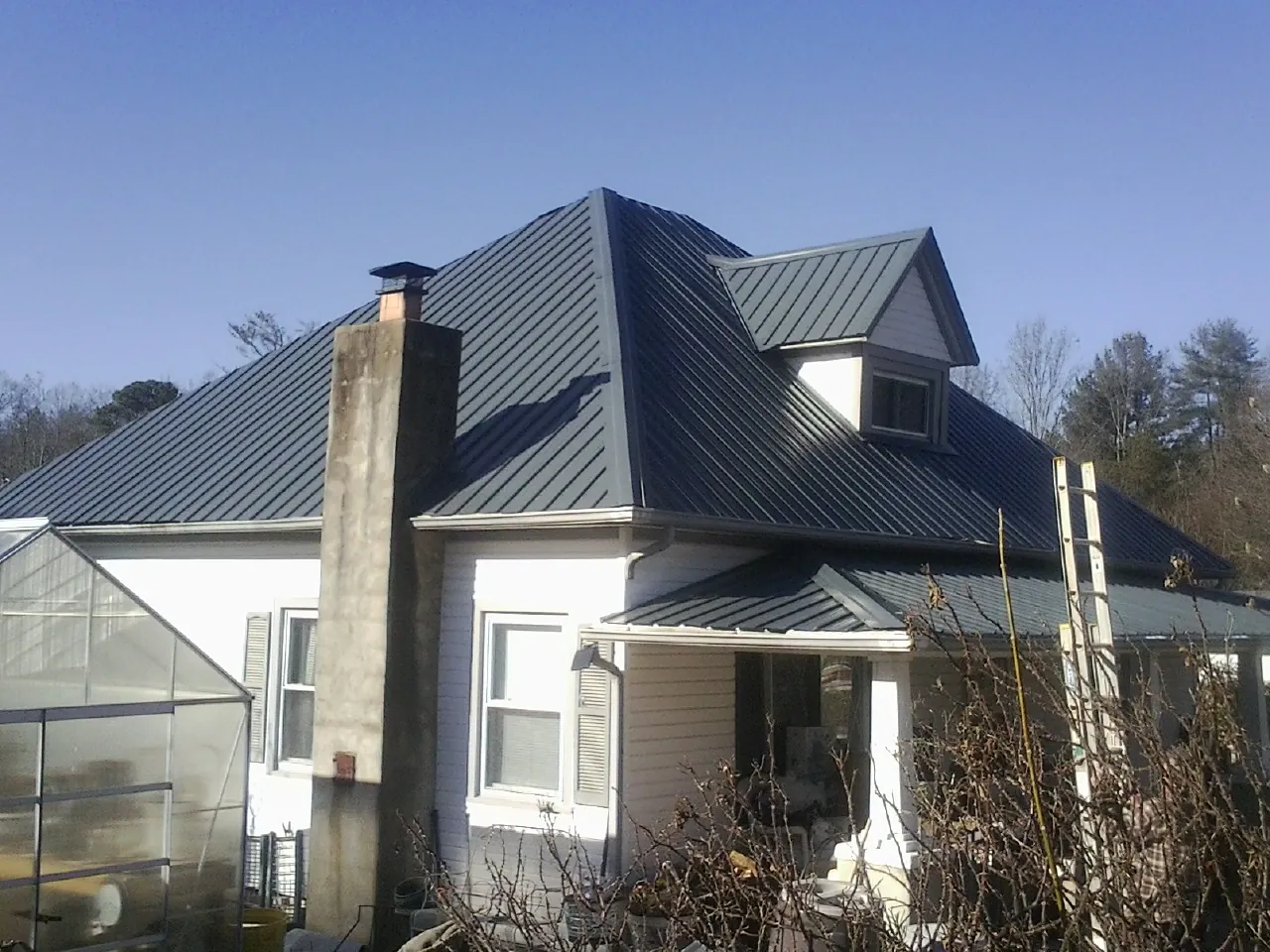Dark blue standing seam metal roof on a white farmhouse with dormer — Slate & Tile Roof Repair by Roofing Brothers in Grundy Center