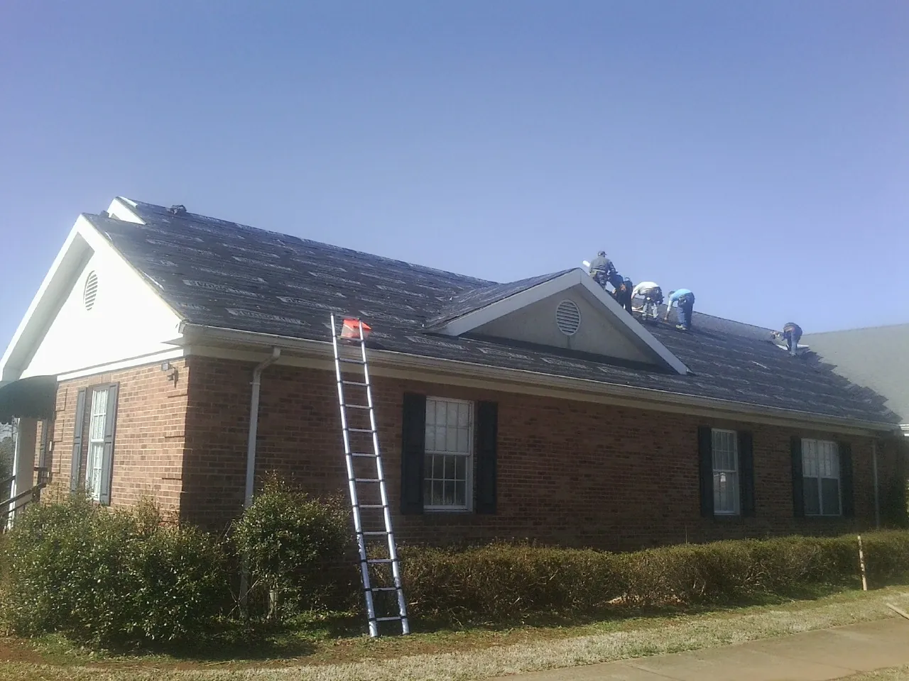 Crew tearing shingles off a brick ranch roof with a ladder set — Metal Roof Repair work by our crew in Grundy Center