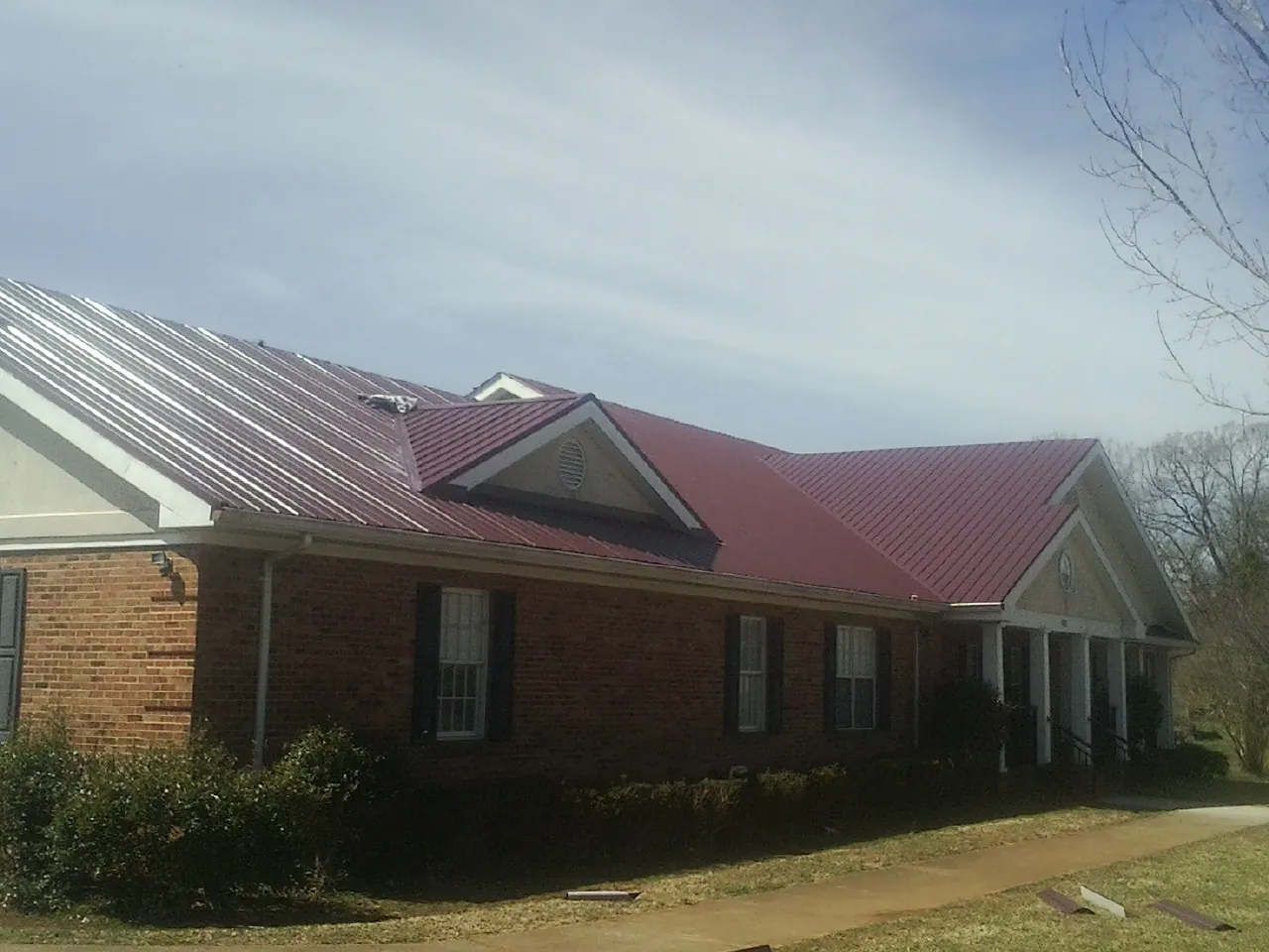 Red metal roof with gabled entries on a long brick building, from a Hail Damage Roof Repair job in Grundy Center