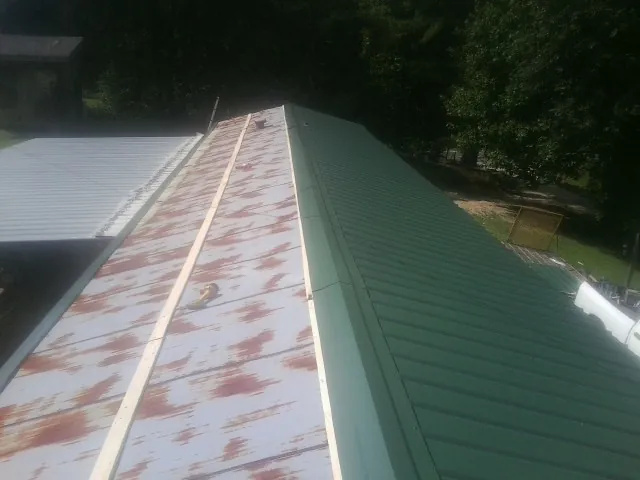 Old rusted panels beside newly installed green metal roofing — Wind Damage Roof Repair by Roofing Brothers in Grundy Center