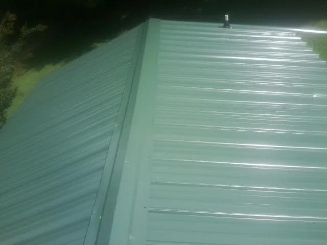 New green metal panels meeting at the ridge of a roof — Flat Roof Repair work by our crew in Grundy Center