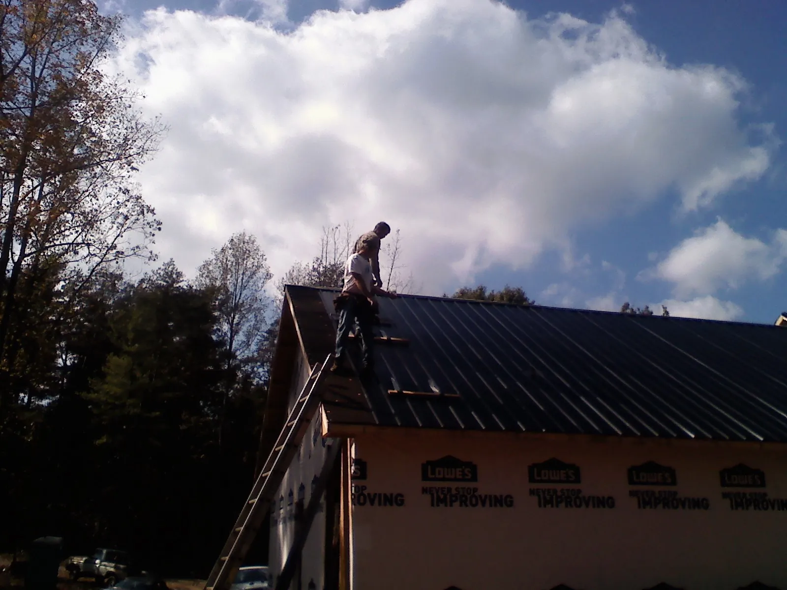 Roofer fastening dark metal panels high against a cloudy sky, from a Roof Inspection job in Grundy Center