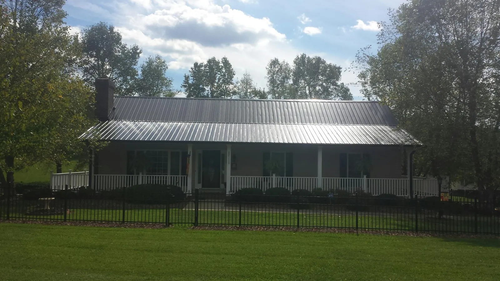 Gray metal roof on a brick ranch with a full width front porch — Gutter Guard Installation work by our crew in Grundy Center