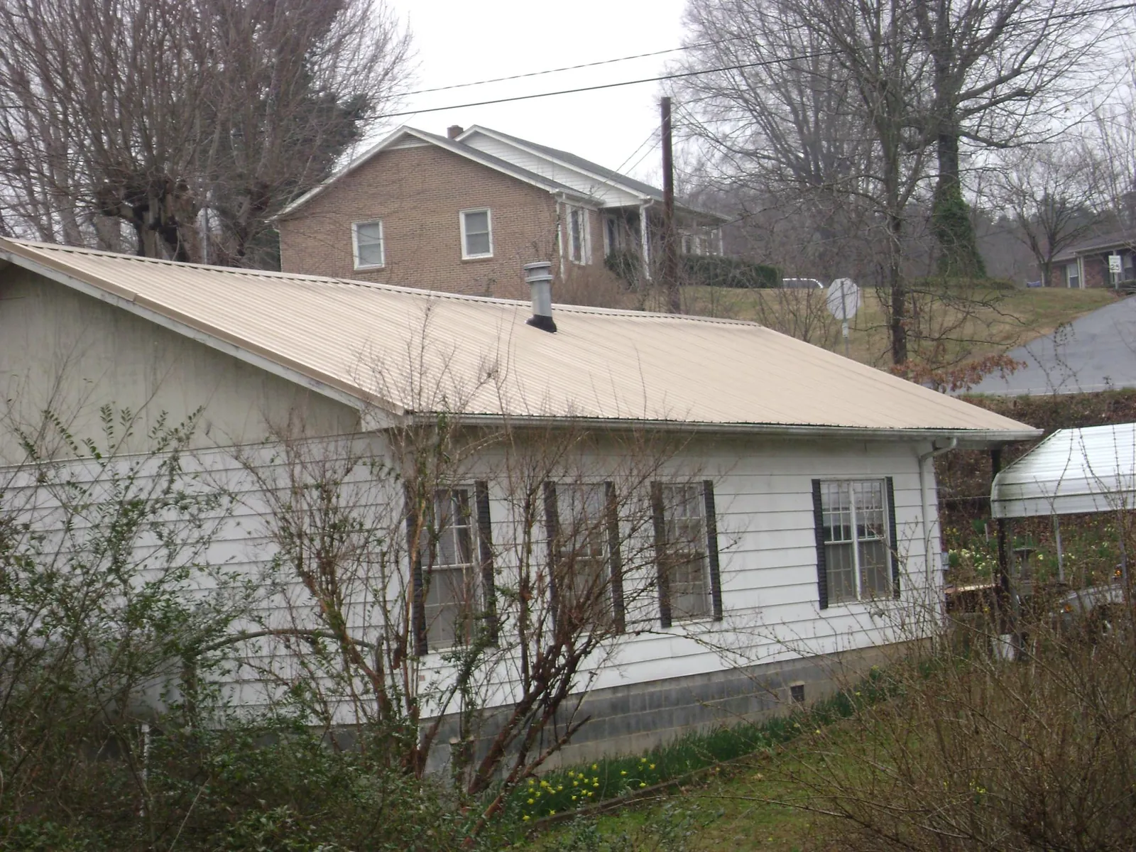 Tan metal roof on a white sided house set into a hillside — Commercial Roofing by Roofing Brothers in Grundy Center