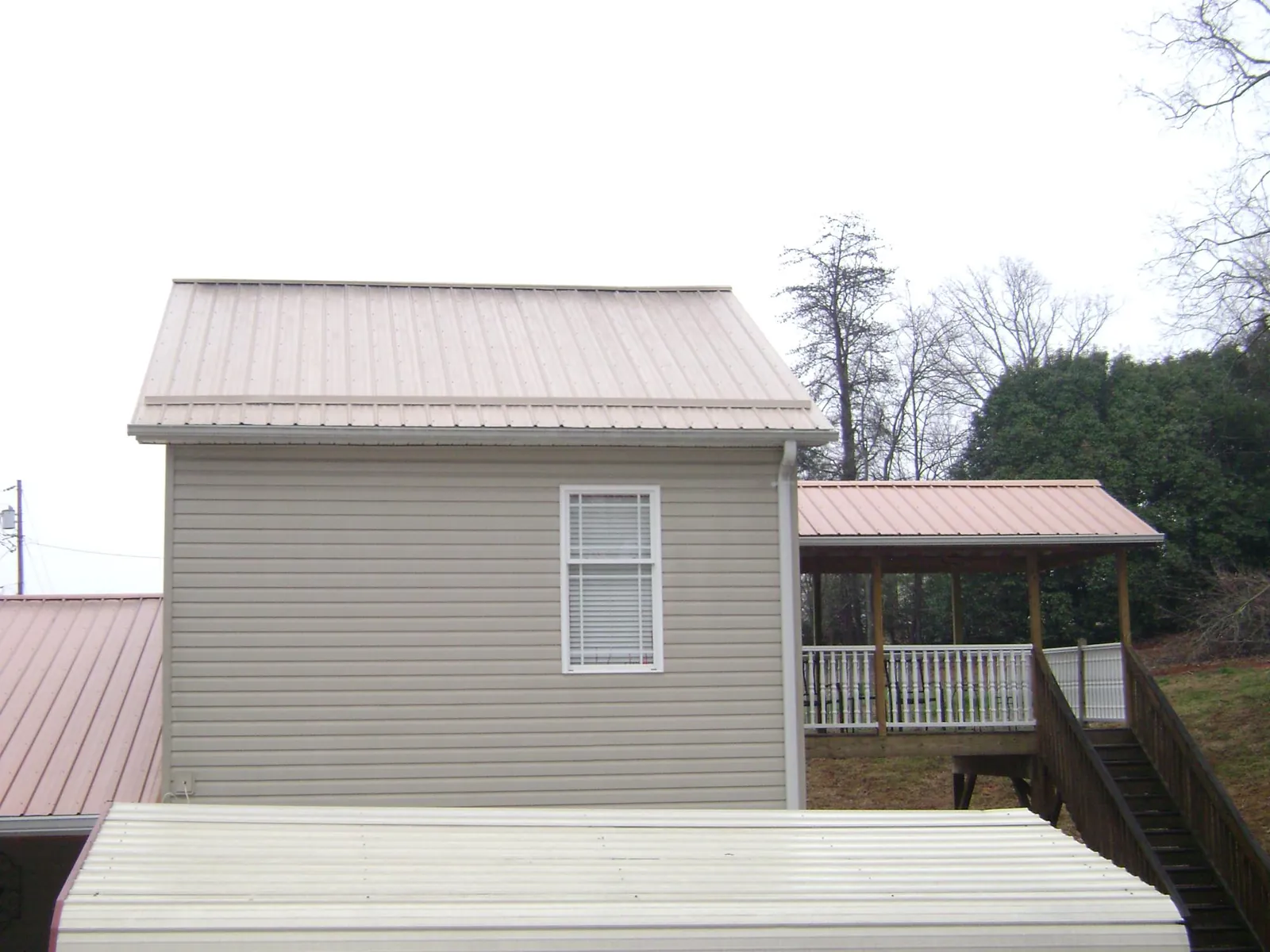 Tan metal roofs on a two story addition and attached porch, from a Roof Replacement job in Grundy Center